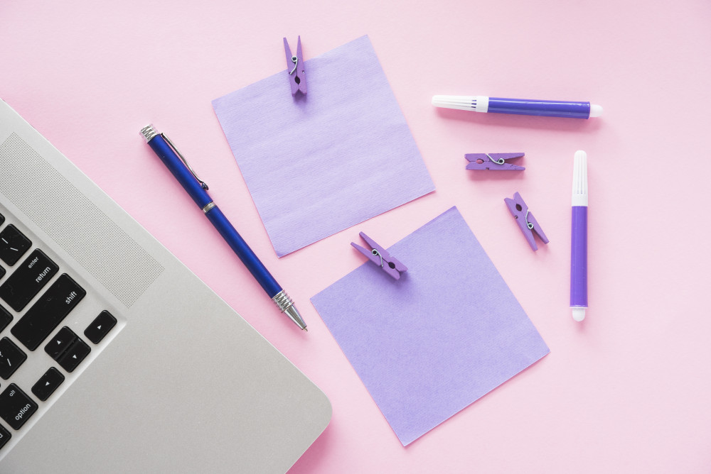 a desk with stick notes, a pen and some colouring pencils, a laptop is seen in the corner