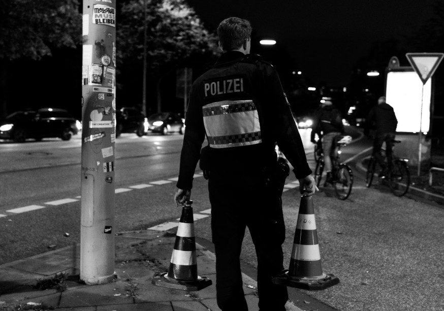 German police officer carrying two traffic cones onto a street