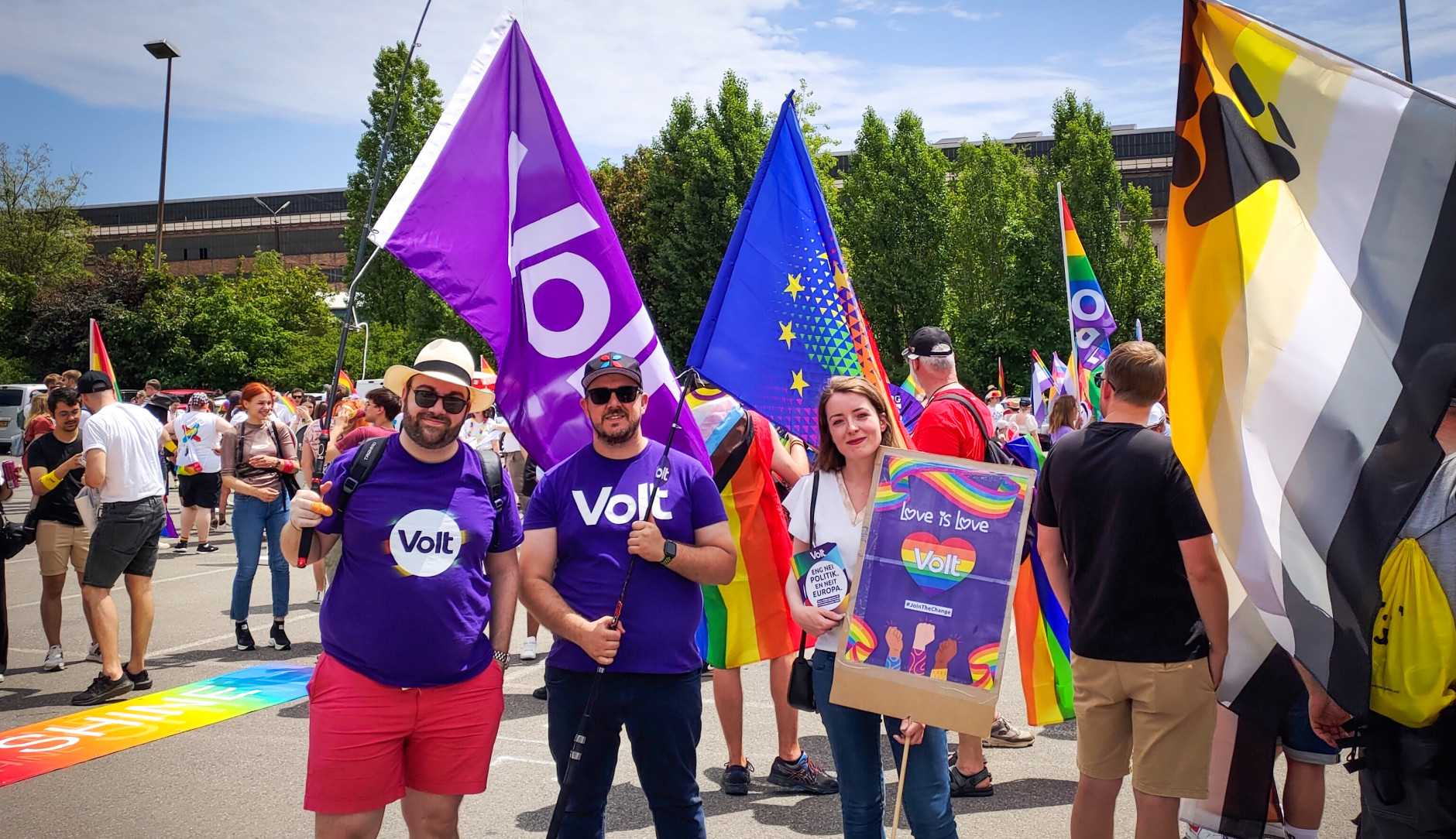 Philippe Schannes holding a Volt flag, Daniel Silva holding a EU/Pride flag and Aurélie Dap holding a poster with 